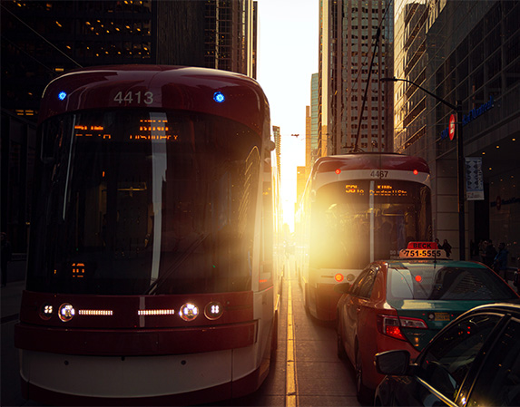 Two trams with the sunsetting between them in the middle of a city.