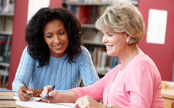 Two people working together at a desk with a notebook in front of them.