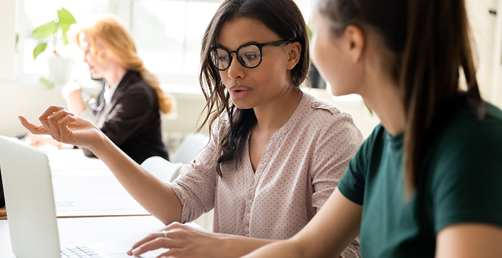 An experienced S-LP shows files to a new grad on a laptop.