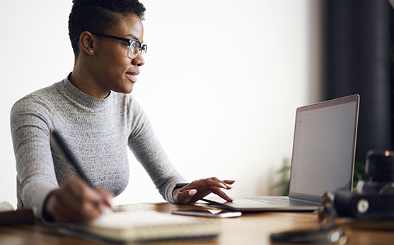 A professional downloads practice resource on their laptop while they take notes