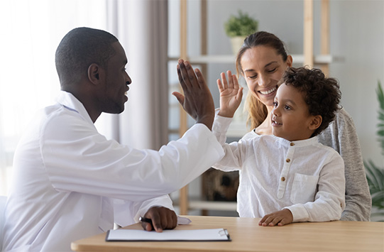 doctor high-fives a child who is sitting on their parent’s lap