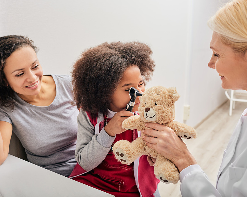 A child looks into a teddy bear’s ear during a visit to the audiology office