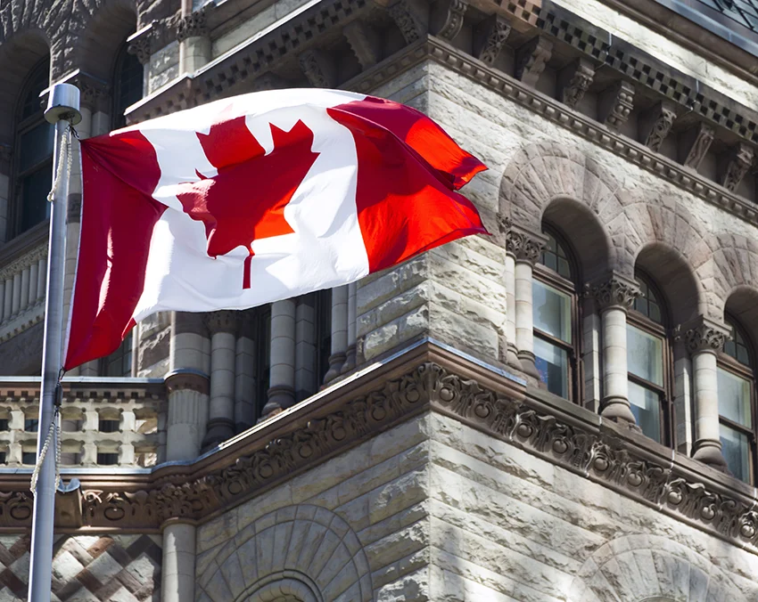 Canadian flag waving in the wind in front of an old stone building with arched windows